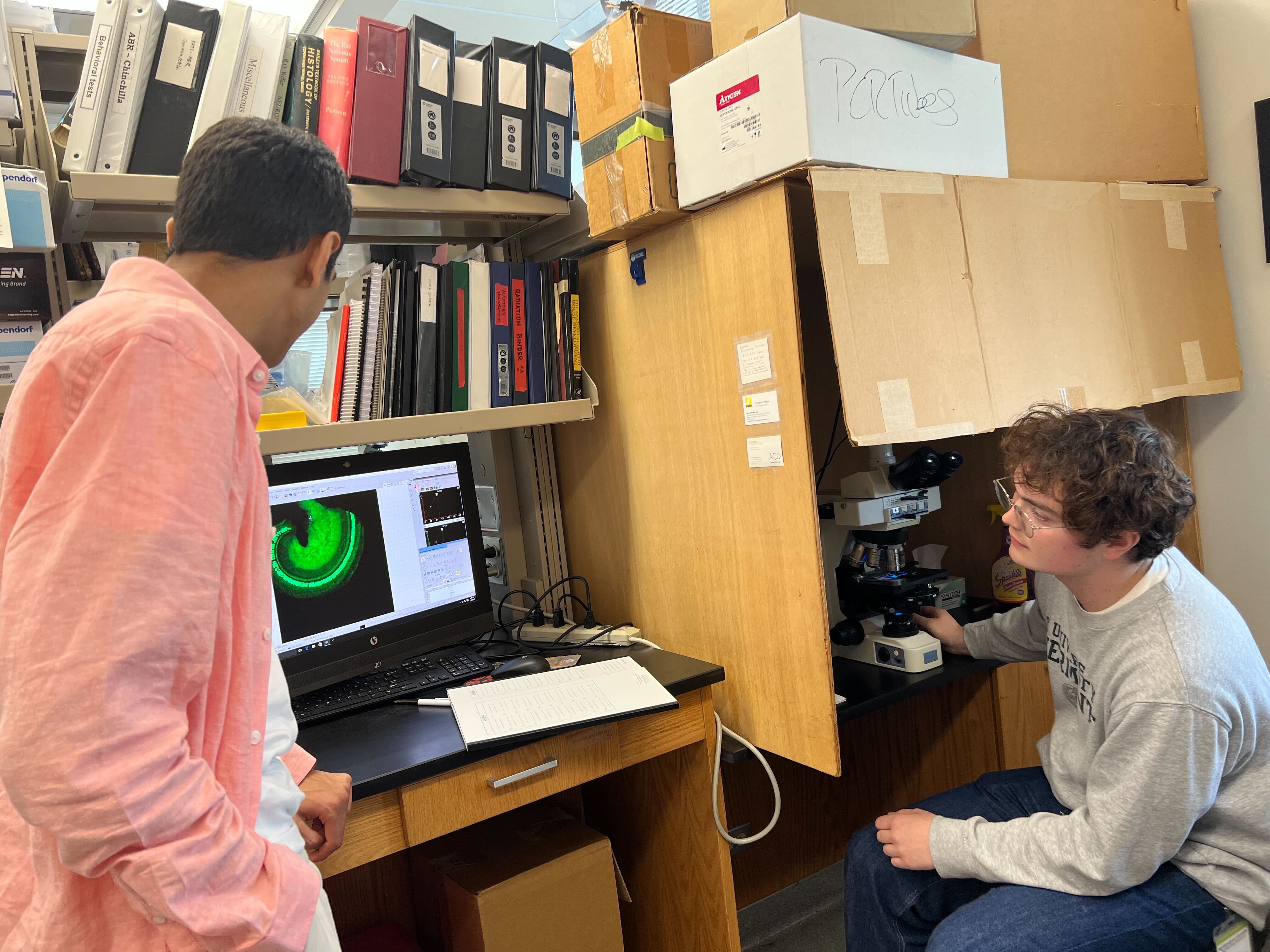 One intern operates a fluorescence microscope while another intern looks at the computer screen