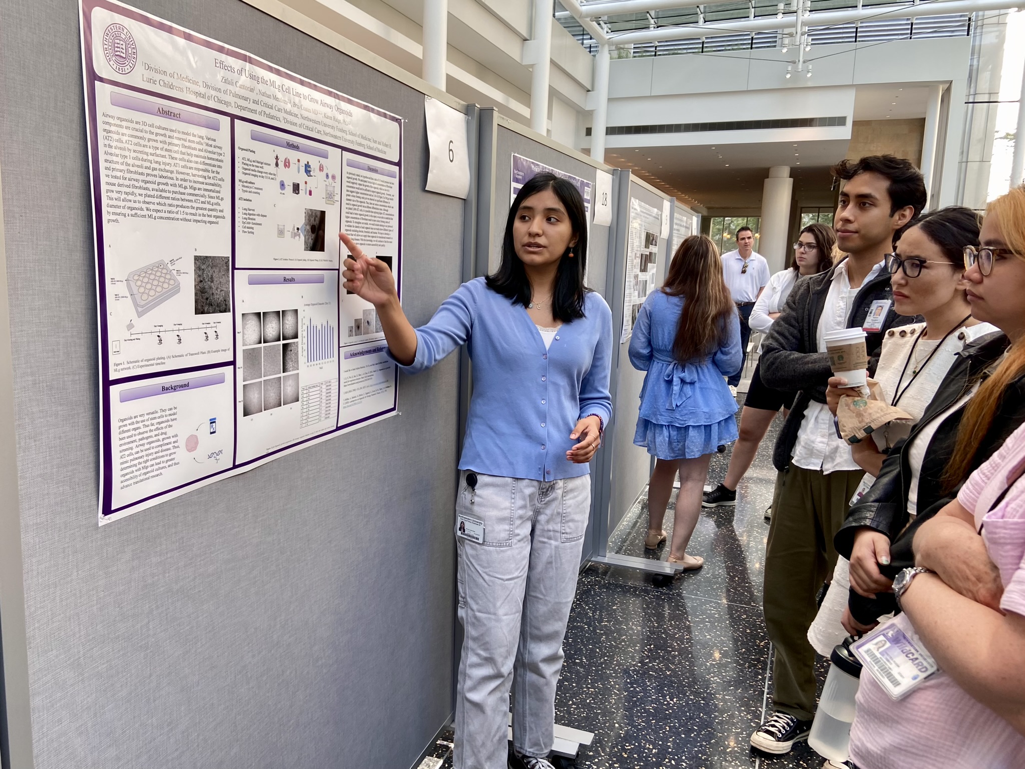 An intern points points to her poster while presenting at the Kimberly Querrey Summer Research Symposium